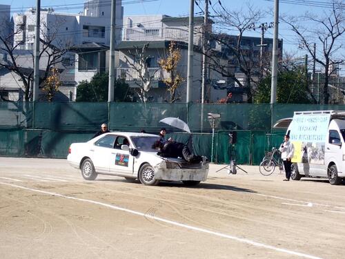 傘さし運転による接触事故をスタントマンが再現している写真
